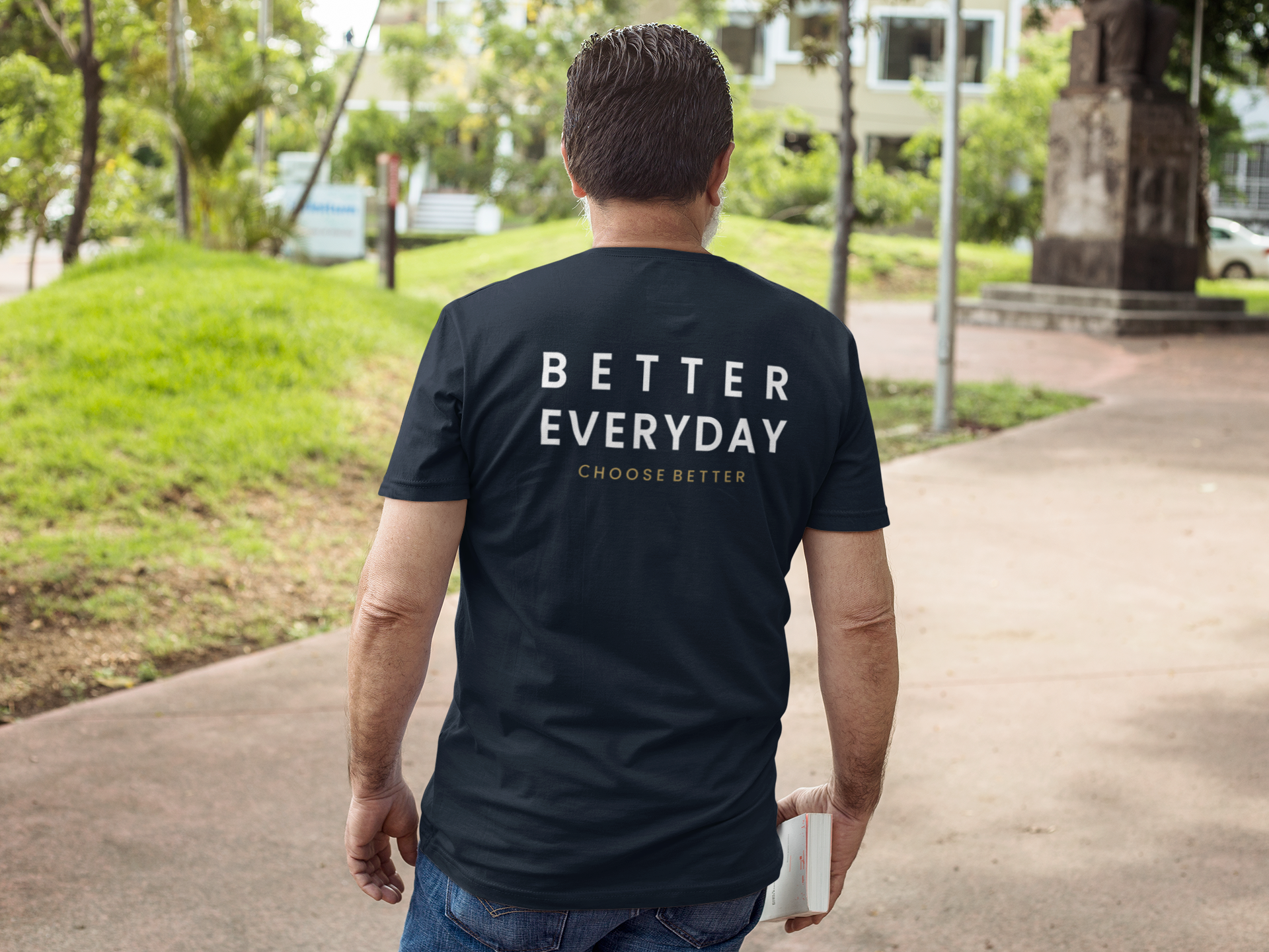 Man wearing a black t-shirt with 'Better Everyday' text walking on a path outdoors.