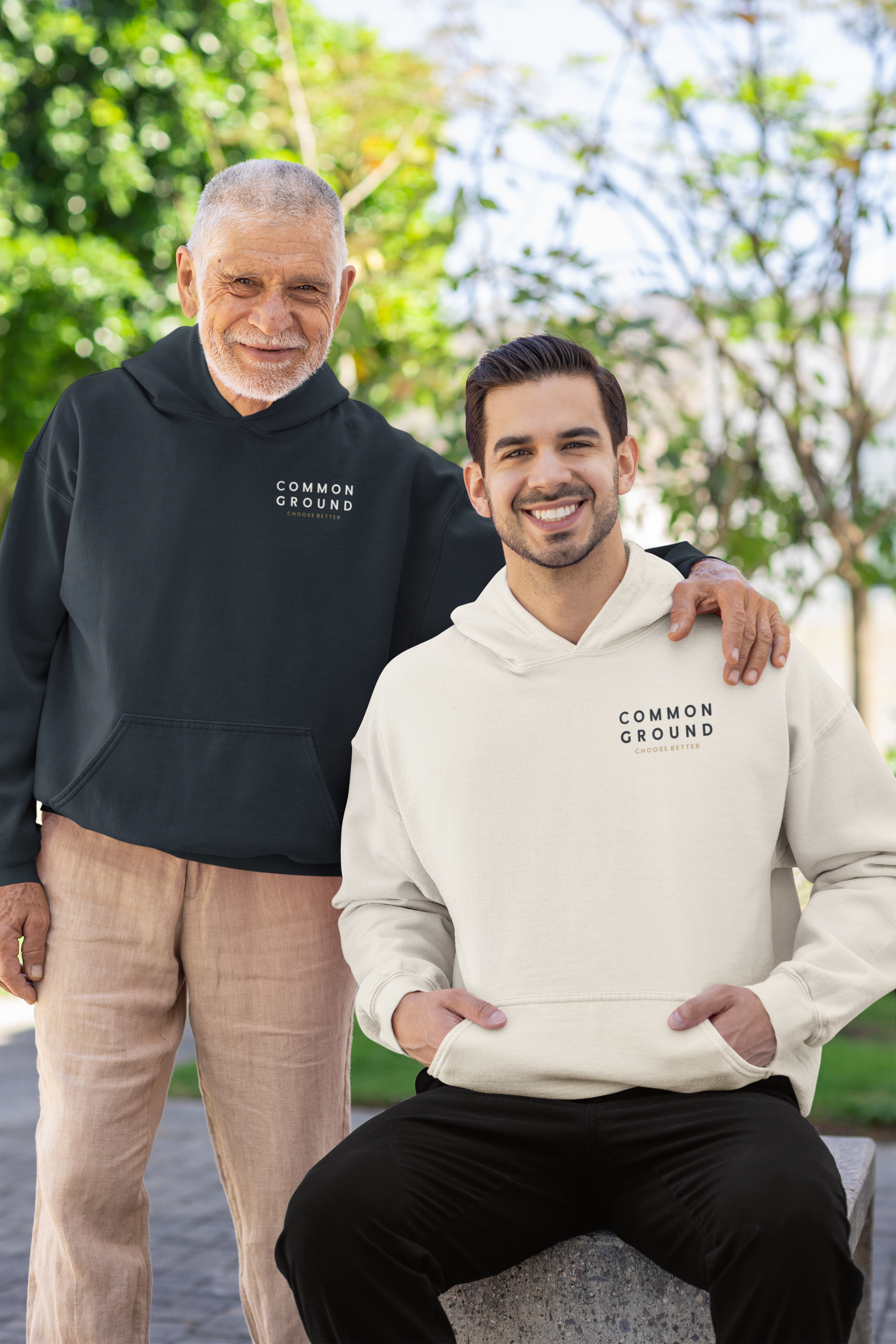 Two people wearing 'Common Ground' hoodies outdoors with trees in the background