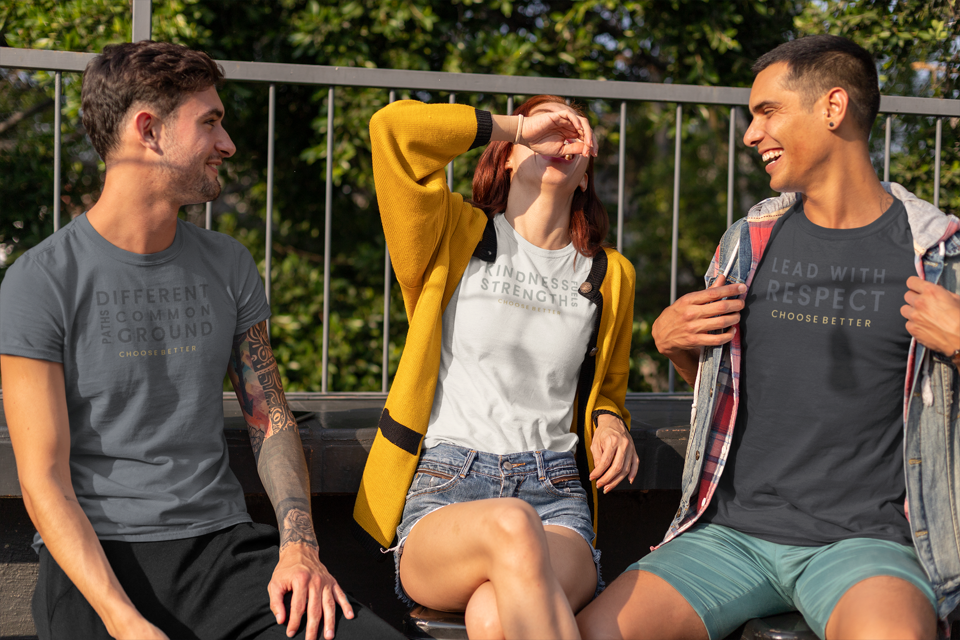 Three young adults sitting outdoors on a bench wearing matching graphic t-shirts with the text 'DIFFERENT STRENGTHS' and 'LEAD WITH RESPECT CHOOSE BETTER'.